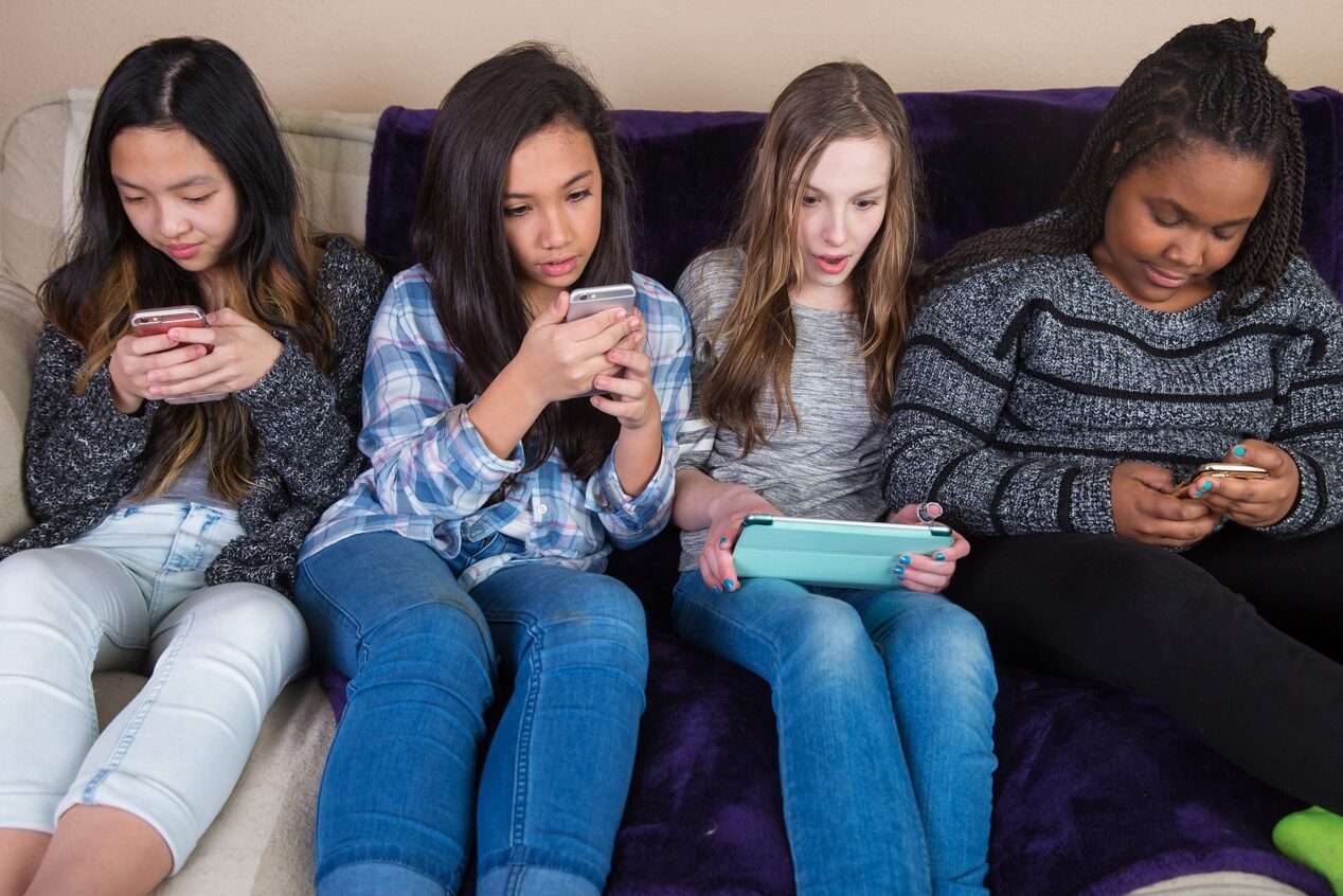 four teen girls glued to their tech devices