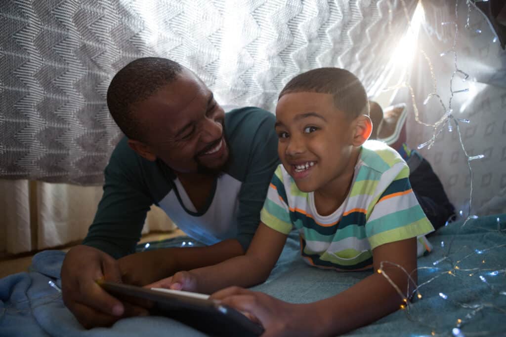 happy father and son in blanket fort looking at tech together