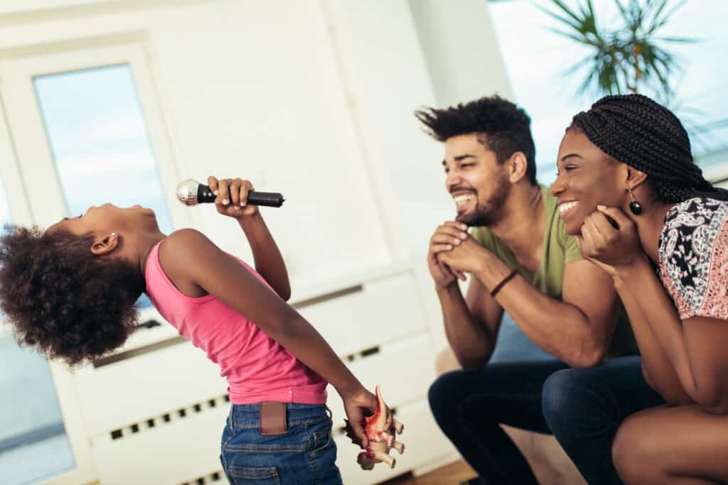 parents smile at their daughter singing out into microphone