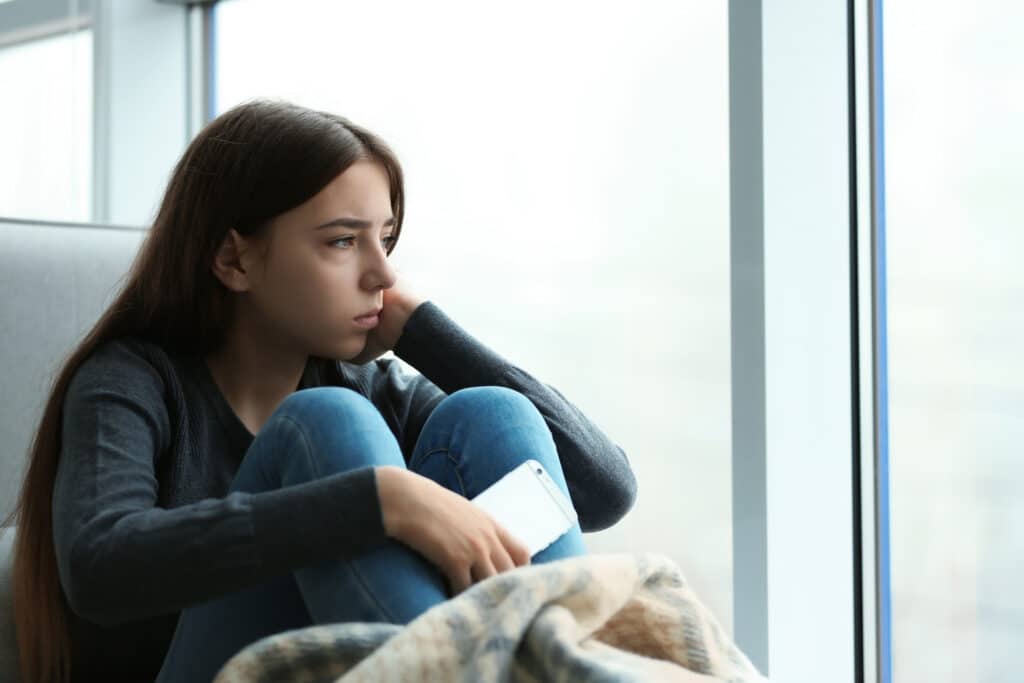 teen girl holding cellphone looks sad