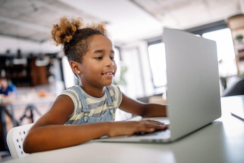 little girl sitting at table with laptop