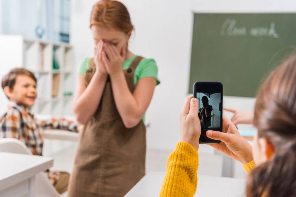 little girl with hands over face being recorded by another student in classroom