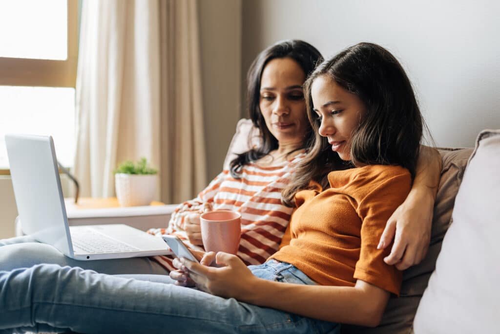 mother with arm around teen daughter as they look at her phone