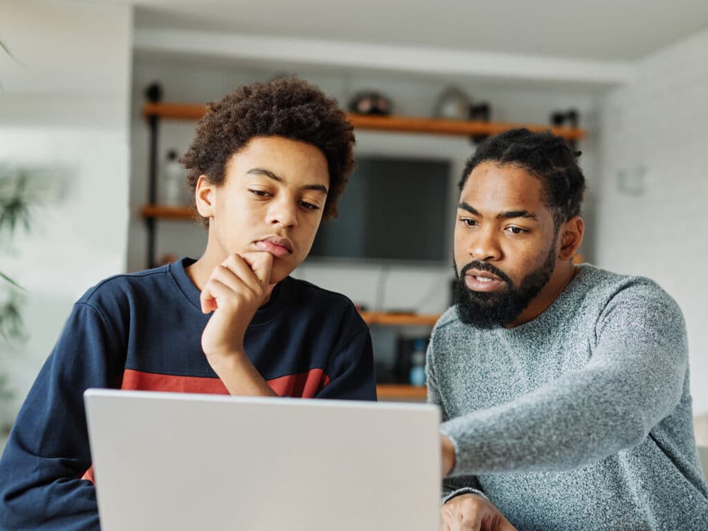 father and son look at a laptop screen together