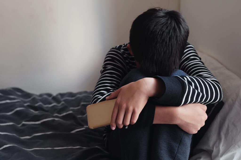 young boy holding phone with head in his arms