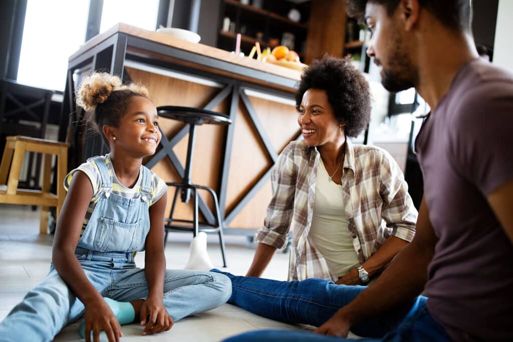 young girl sitting on floor with her parents smiling