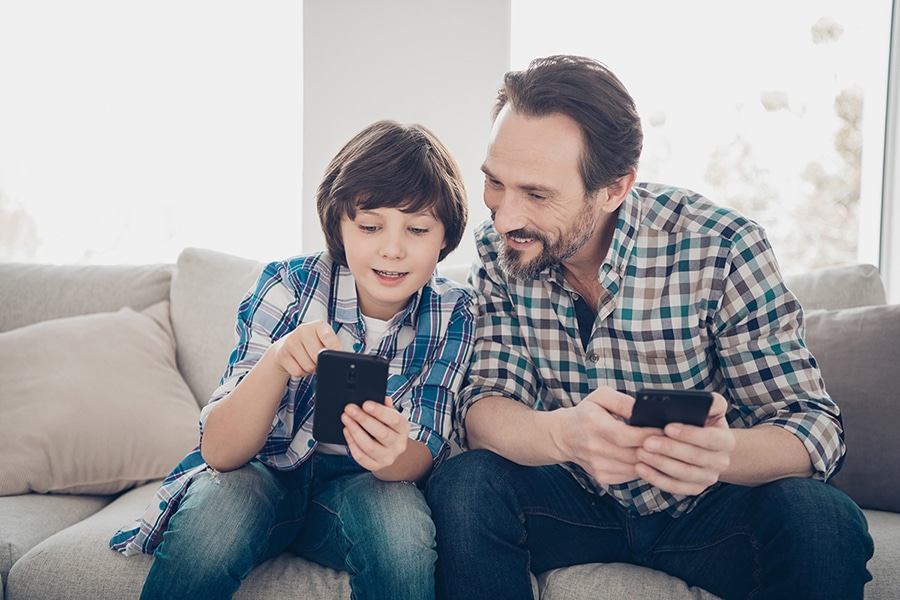 father and son smiling at phones