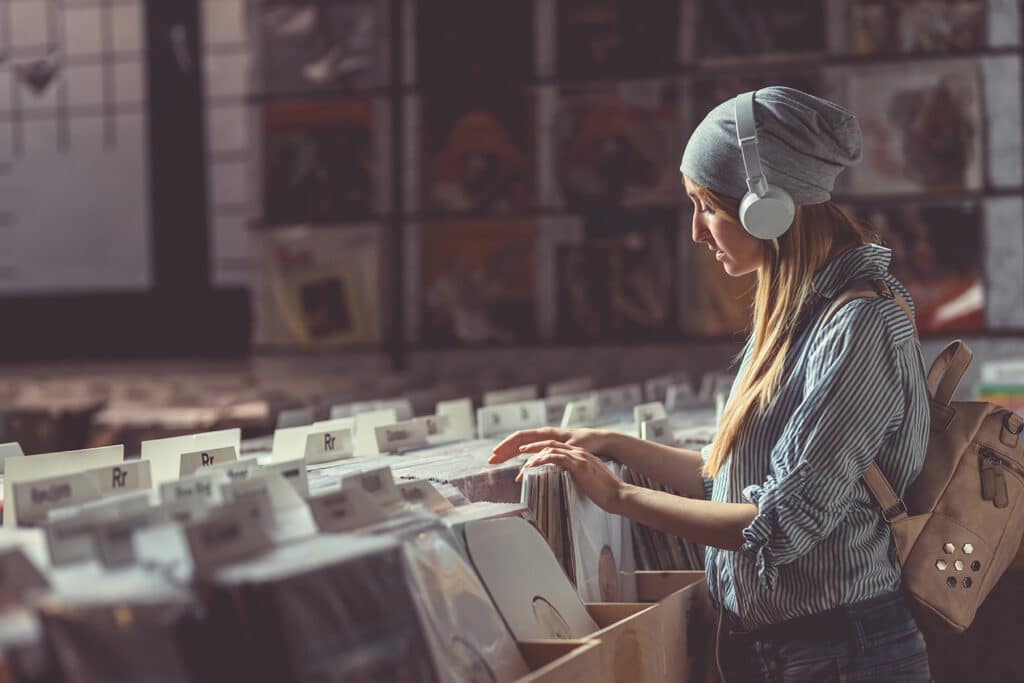 teen girl with headphones on looking through records at a record store