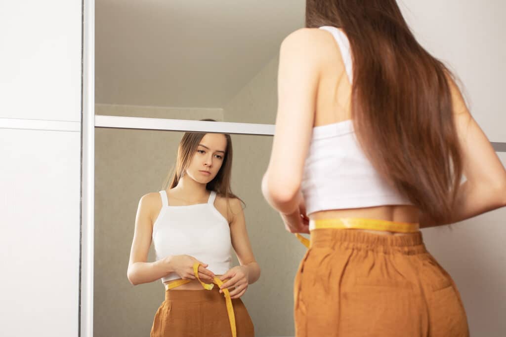 young girl measuring her waist in the mirror