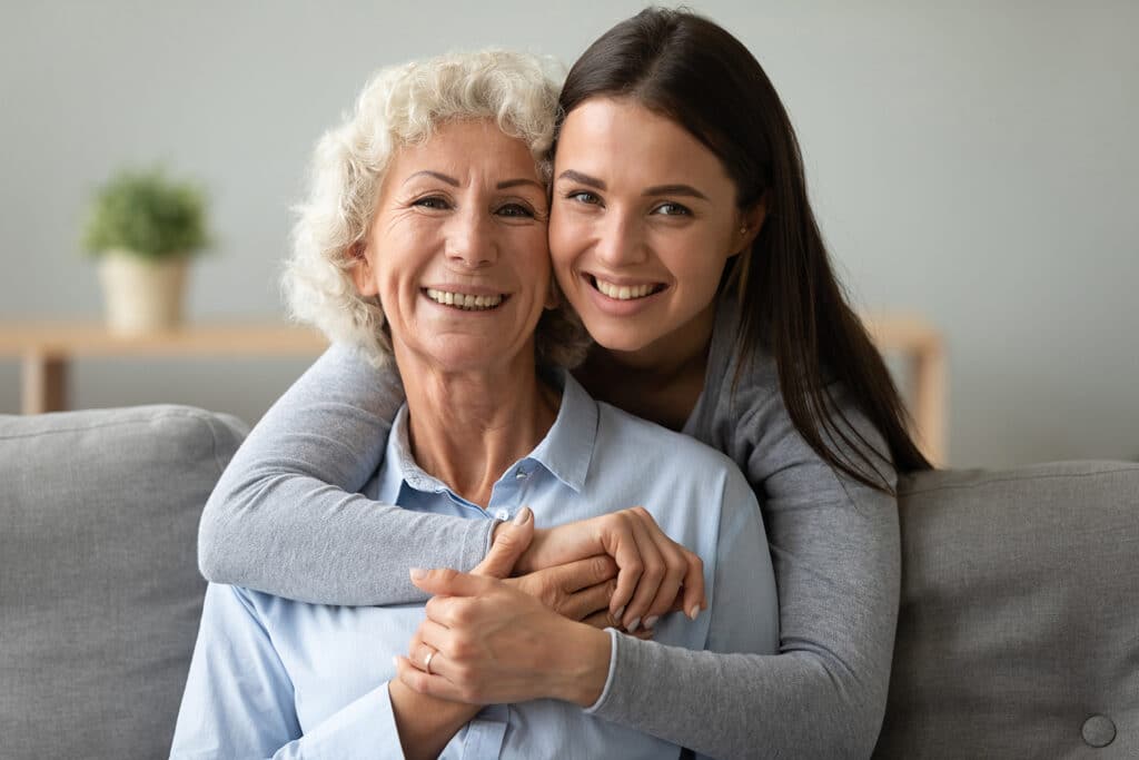 young woman hugging older woman from behind both smiling