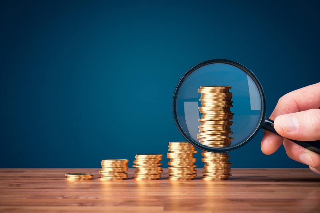 five stacks of coins with the largest stack having a magnifying glass