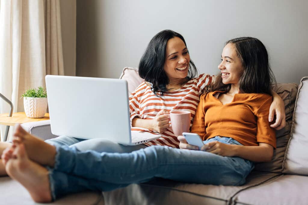 mother with arm around daughter smiling both holding tech