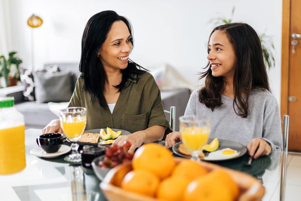 mother and daughter smiling at each other over breakfast