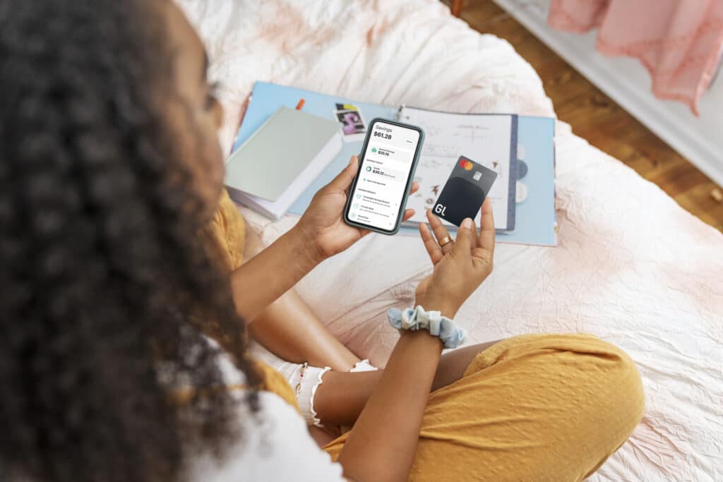 teen girl holding cell phone with greenlight app and greenlight credit card