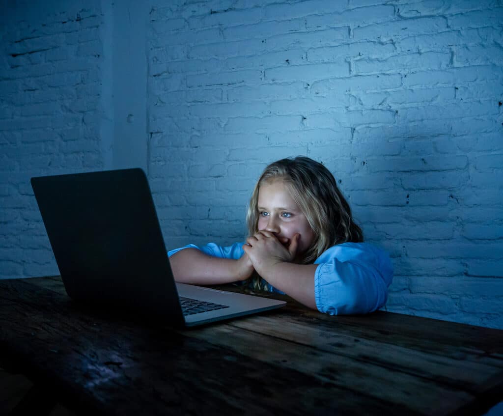 young girl in dark room lit up by computer screen