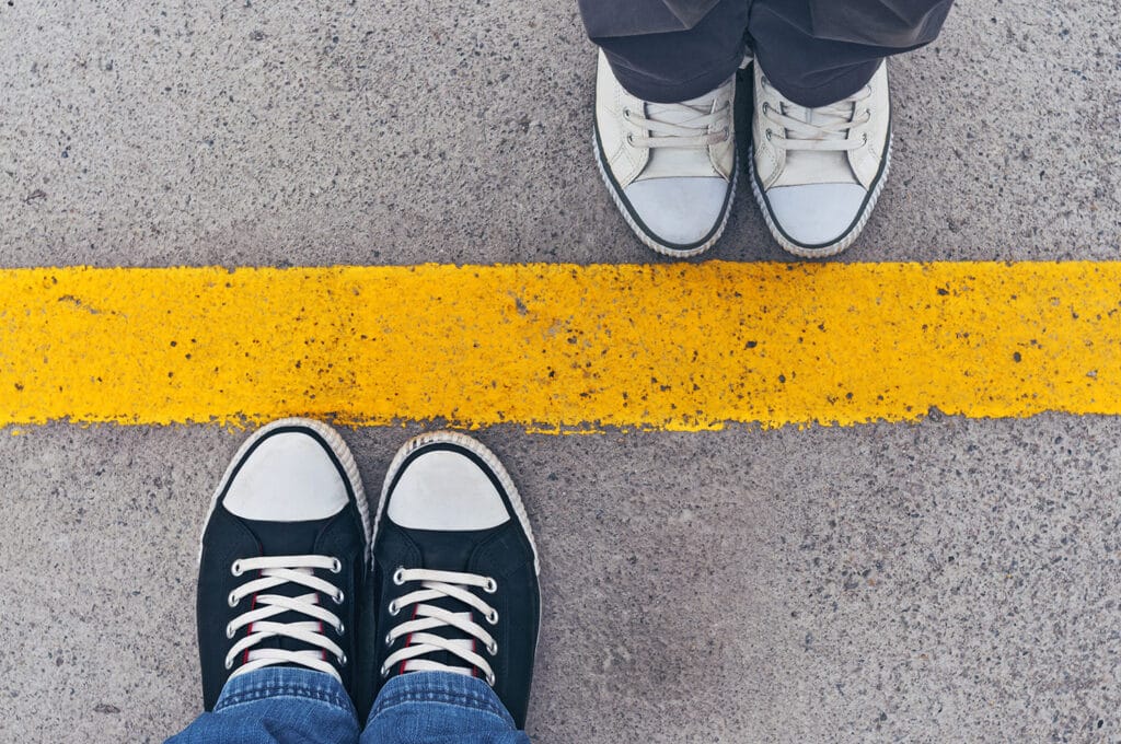 picture of two pairs of legs and feet on opposite side of a yellow line